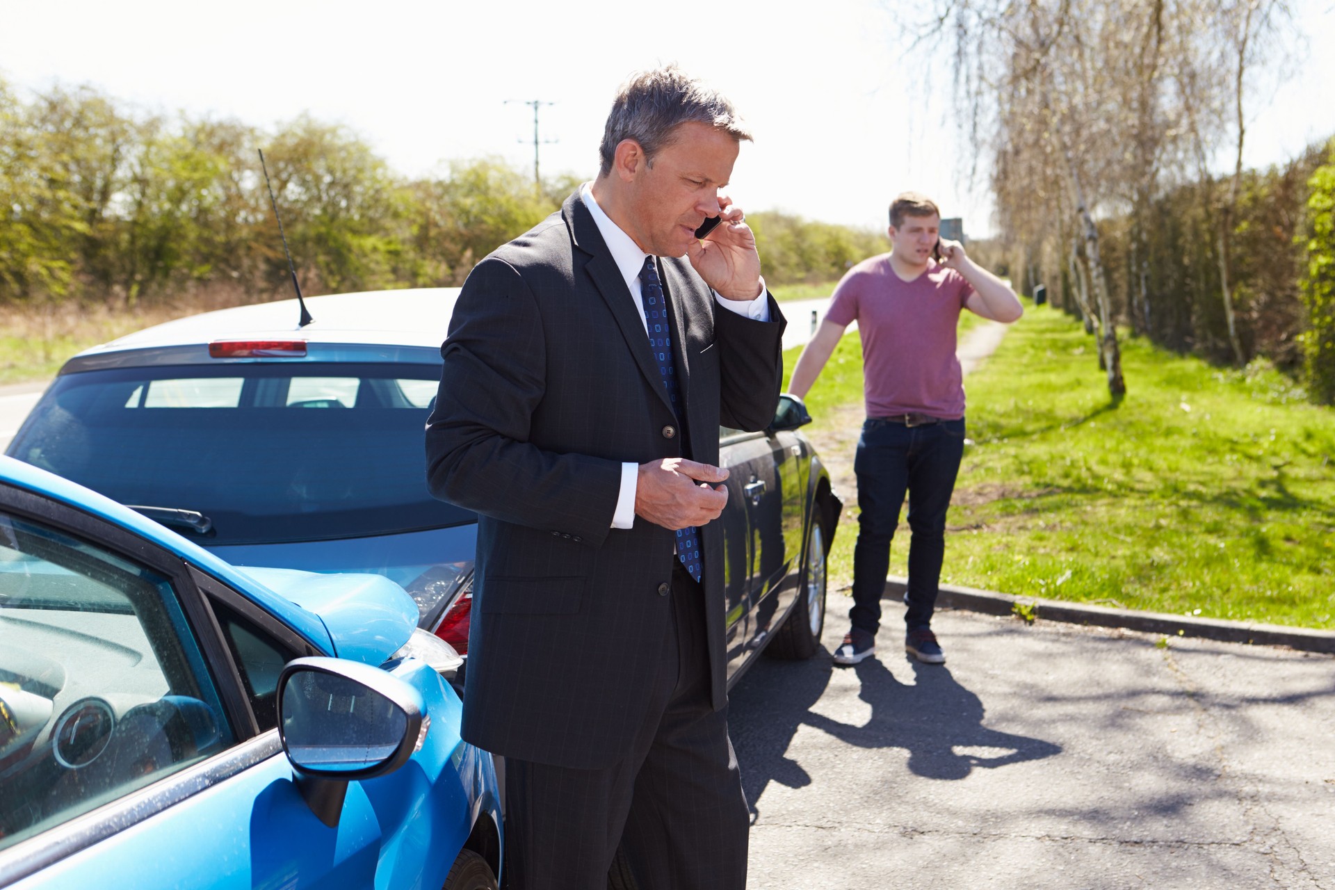 Two men making phone calls after a car accident